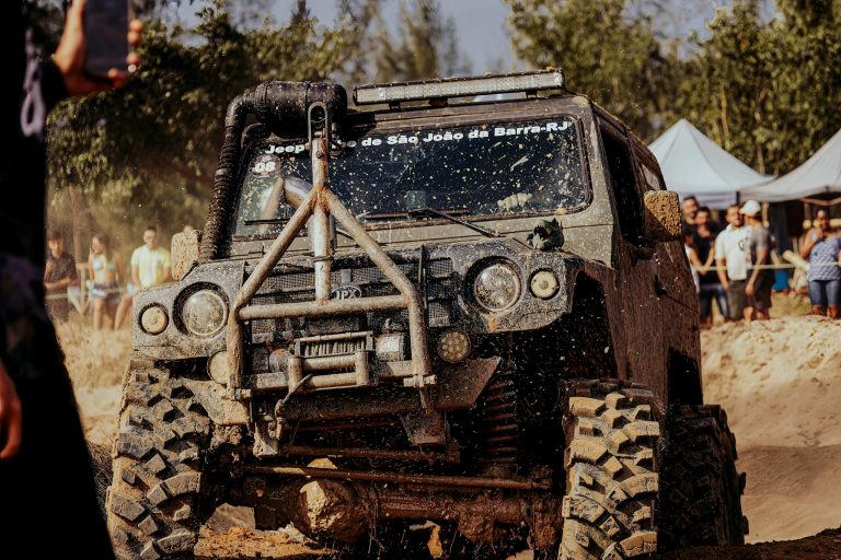 Jeep overcoming muddy terrain at off-road event with spectators watching in the background.